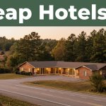 A modest roadside motel with glowing rooms surrounded by pine trees and an empty highway at sunset.