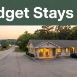 A roadside budget motel with glowing windows along a quiet rural highway at sunset.