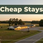 A modest roadside motel with warm lights glowing at dusk near rural farmland.