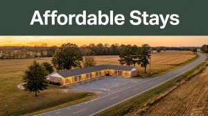 A modest roadside hotel glows in the golden light beside a quiet rural highway and farmland.
