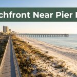 A beachfront hotel and walkway lead toward a pier and distant buildings.