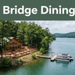A lakeside restaurant patio with a dock, calm water, and wooded shoreline.