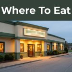 A glowing roadside restaurant entrance beside a highway at dusk, with a green “Where To Eat” banner.