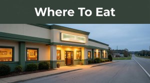 A glowing roadside restaurant entrance beside a highway at dusk, with a green “Where To Eat” banner.