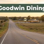 A rural Arkansas road leads toward a warmly lit restaurant at sunset.