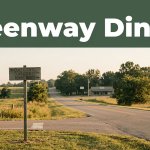 A rural Arkansas crossroads with a directional sign and distant café in morning light.