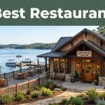 A rustic restaurant with warm windows, patio seating, and boats on calm lake water.