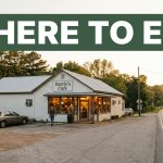 A warmly lit diner beside a rural road with a Where To Eat banner.