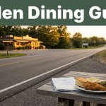 A comfort-food plate and road map overlook a highway leading to a lit diner at sunset.