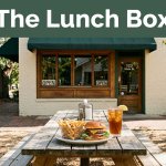 A small restaurant with a burger lunch on a picnic table outside.