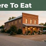 A small brick restaurant with glowing windows and a clean parking area at dusk.