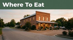 A small brick restaurant with glowing windows and a clean parking area at dusk.