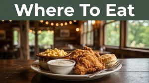 Plated Southern food sits on a wooden table with a farmhouse restaurant and leafy Ozark scenery behind it.