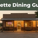 A warmly lit diner with an OPEN sign, parked pickups, and a green guide banner at sunset.