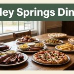A rustic table holds barbecue, sides, pizza, and pie beside an Arkansas countryside view.