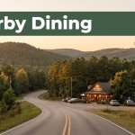 A country road leads to a warmly lit café beneath pine-covered hills.