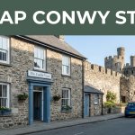 A modest Conwy guesthouse with a parked car and castle walls behind it.