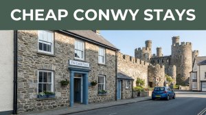 A modest Conwy guesthouse with a parked car and castle walls behind it.