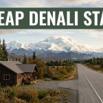 A roadside lodge and highway lead toward snowy Denali mountains in morning light.