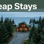 A warm cabin beside spruce trees and the Alaska coast under an overcast sky.