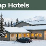A modest hotel with warm windows, snowy trees, mountains, and a parked car near Fairbanks.