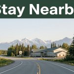 A roadside hotel beside an Alaska highway with spruce trees and snow-dusted mountains.