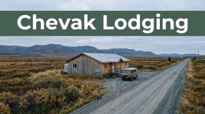 A wooden guesthouse and van beside a gravel road in the Alaskan tundra.