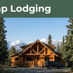 A warmly lit cabin beside a parked vehicle, spruce trees, and snowy mountains.