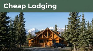 A warmly lit cabin beside a parked vehicle, spruce trees, and snowy mountains.