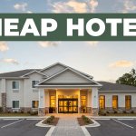 Budget hotel entrance with parking and pine trees at sunset.