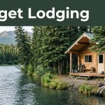 A rustic cabin beside an Alaskan river with fishing gear, spruce trees, and distant mountains.