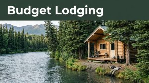 A rustic cabin beside an Alaskan river with fishing gear, spruce trees, and distant mountains.