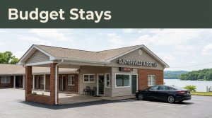 Budget motel exterior with a parked car, lake scenery, and a Budget Stays banner.
