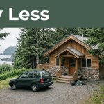 An Alaska cabin with an SUV, fishing gear, spruce trees, and a rugged coastline.