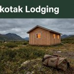 A warm-lit cabin with a duffel bag, tundra, mountains, and an overcast sky.