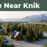 A rustic lodge beside the Knik River with mountains and a green “Save Near Knik” banner.