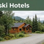 A cozy cabin lodge beside a road in a spruce forest with mountains behind it.