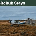 A bush plane beside a cabin on flat Alaska tundra beneath a slate-blue sky.
