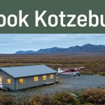 A warm-lit lodge and bush plane sit beneath an overcast Alaskan sky.