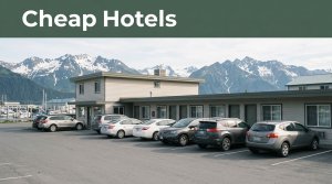 A roadside motel with parked cars, harbor water, and mountains near Seward, Alaska.