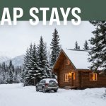 Wood cabin with warm windows beside a snowy road, spruce trees, mountains, and a parked vehicle.