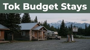 A roadside cabin, travel vehicle, fuel sign, and spruce trees near Tok, Alaska.