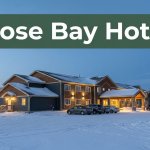 A warmly lit hotel with parked cars sits in snowy Goose Bay beneath a twilight sky.
