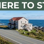 A coastal hotel beside rocky shore in St. Anthony under a green Where To Stay banner.