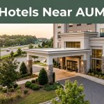 A landscaped hotel entrance at sunset with a dark-green Hotels Near AUM banner.