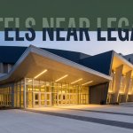Legacy Arena entrance with a nearby hotel under a dark-green headline band at blue hour.