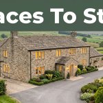 Stone inn with glowing windows beside green countryside and a neat driveway.