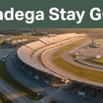 Talladega Superspeedway and grandstands sit beside a curving highway and distant hotels.