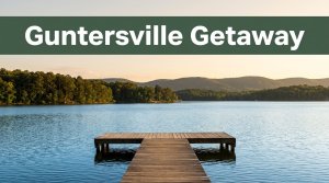 A wooden dock leads across Lake Guntersville toward wooded shores and distant foothills at sunset.