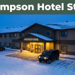 Snow surrounds a lit Manitoba hotel entrance and parked SUV.